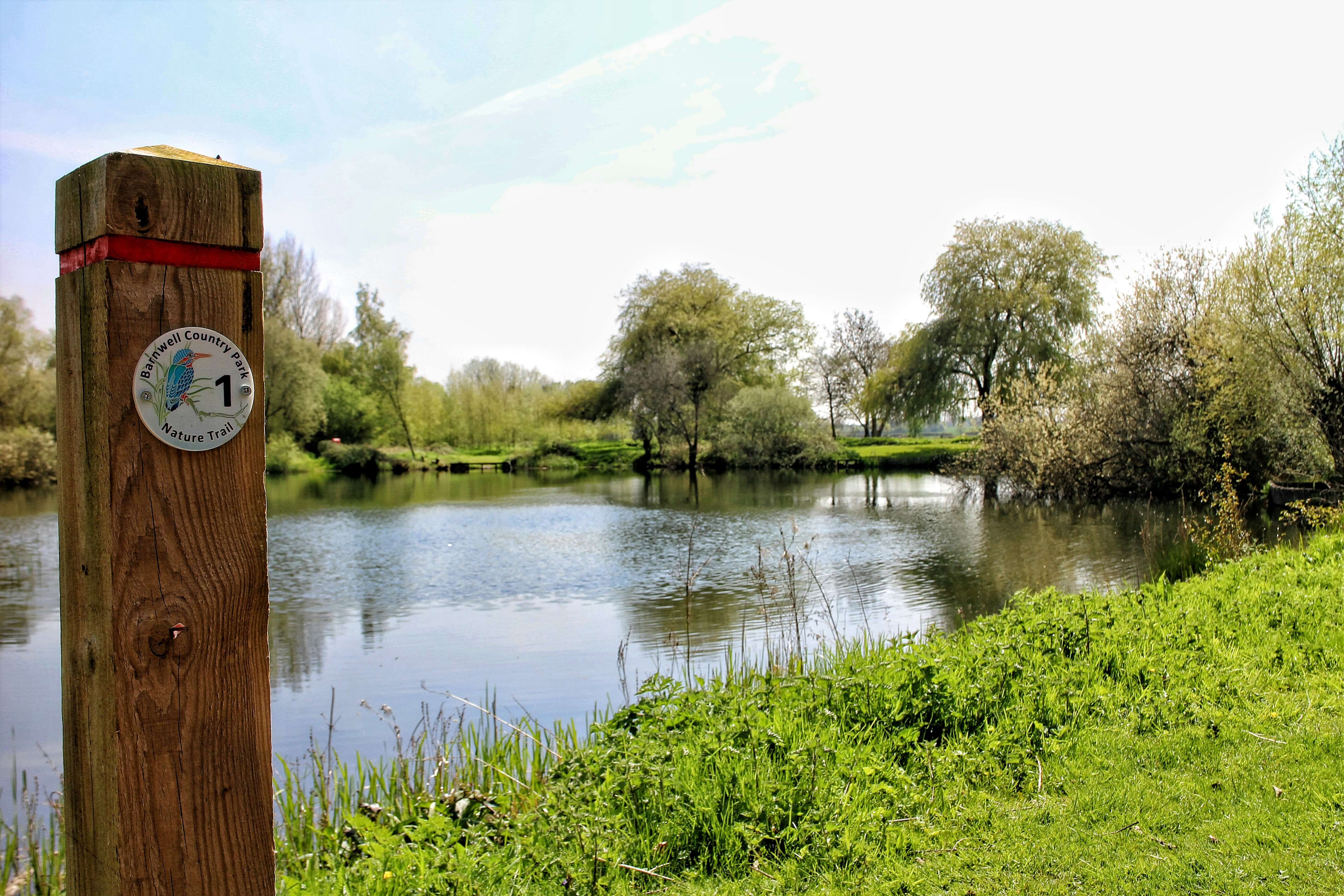 A sign indicating the nature trail at Barnwell Country Park, a lake is in the background